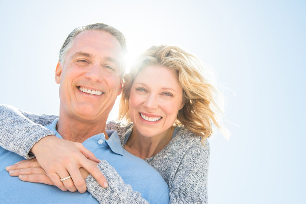 Cheerful Woman Embracing Man From Behind Against Sky