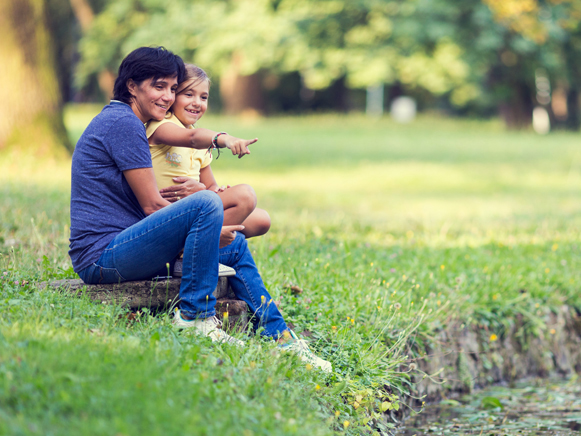 Mother With Child Pointing To A Pond Sitting Outdoors