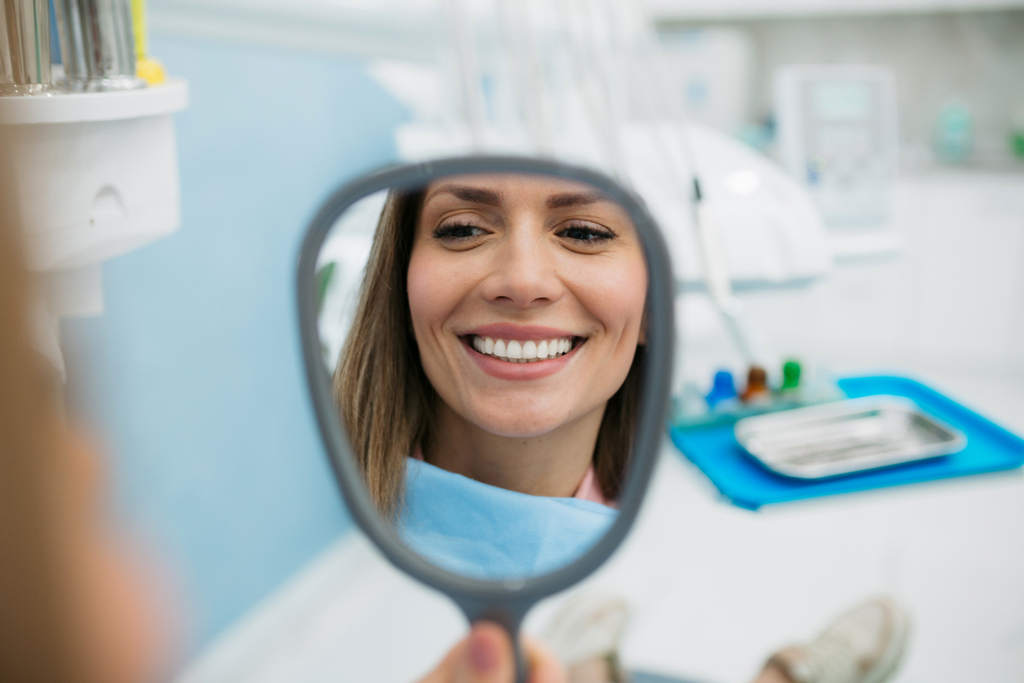 Woman In Dentist Office Smiling Looking In Mirror
