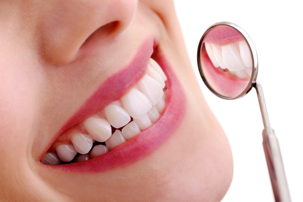 Close up of the smile of a woman being examined with a small dental mirror