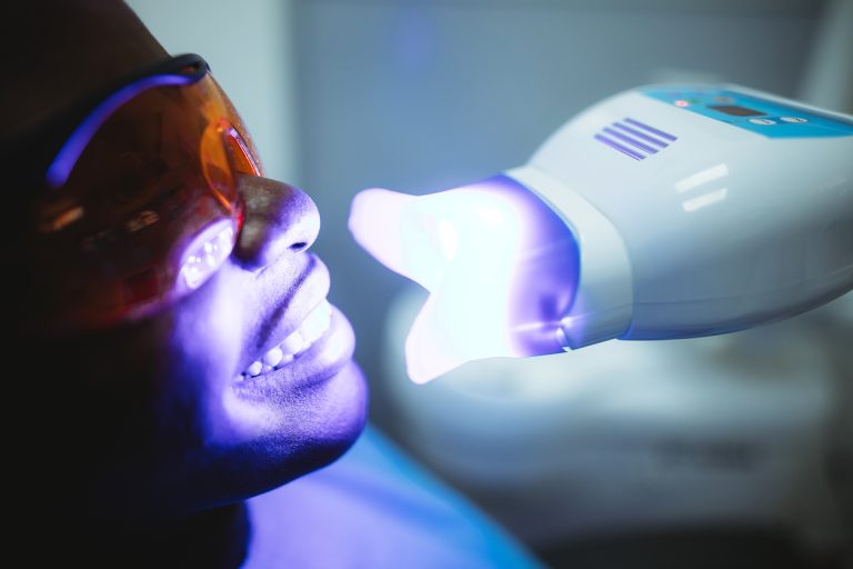 Cosmetic dental patient receiving professional teeth whitening while wearing protective glasses